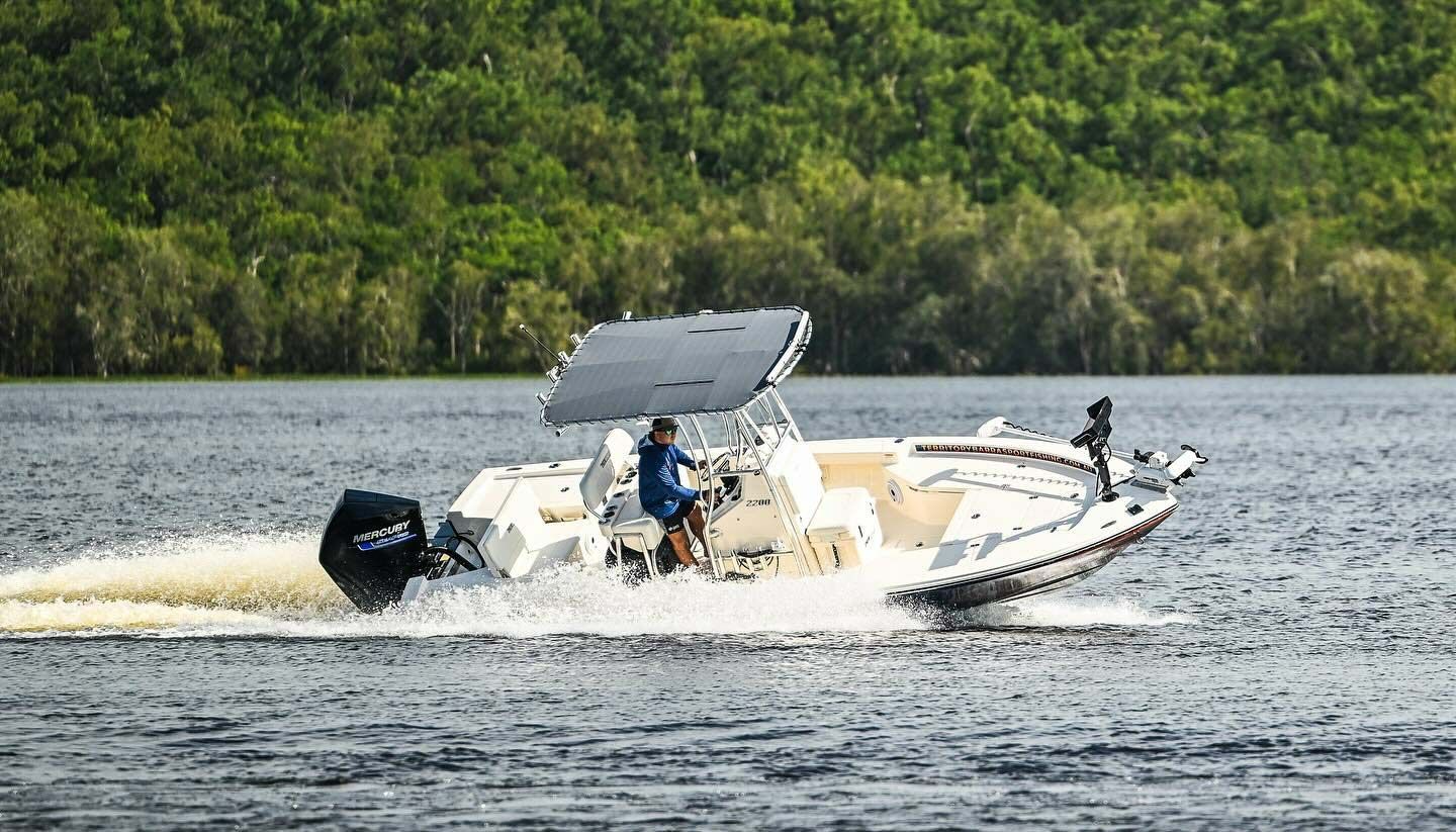 A Man Is Driving A Boat On A Lake With Trees In The Background — Territory Barra Sportfishing In Zuccoli, NT