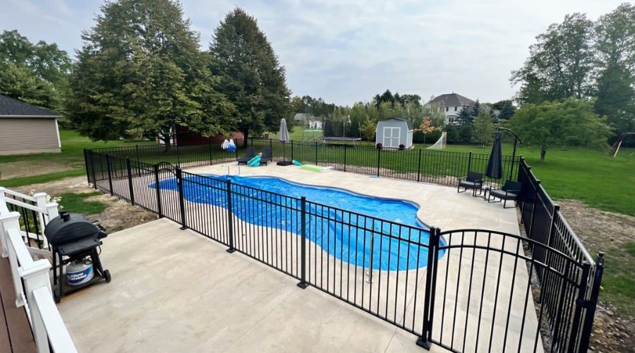Black metal pool fence installation surrounding an in-ground pool patio in a large backyard.