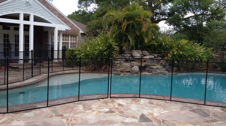 Removable black mesh pool fence installed on a flagstone patio next to a stone waterfall feature.