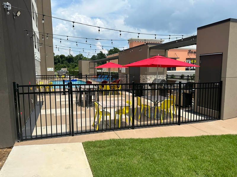 A fence surrounds a patio area with tables and chairs and umbrellas.