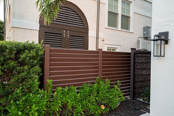 A brown fence is in front of a white house.