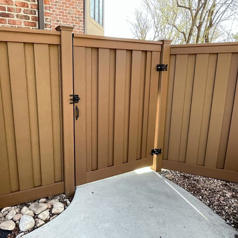 A wooden fence with a gate and a brick building in the background