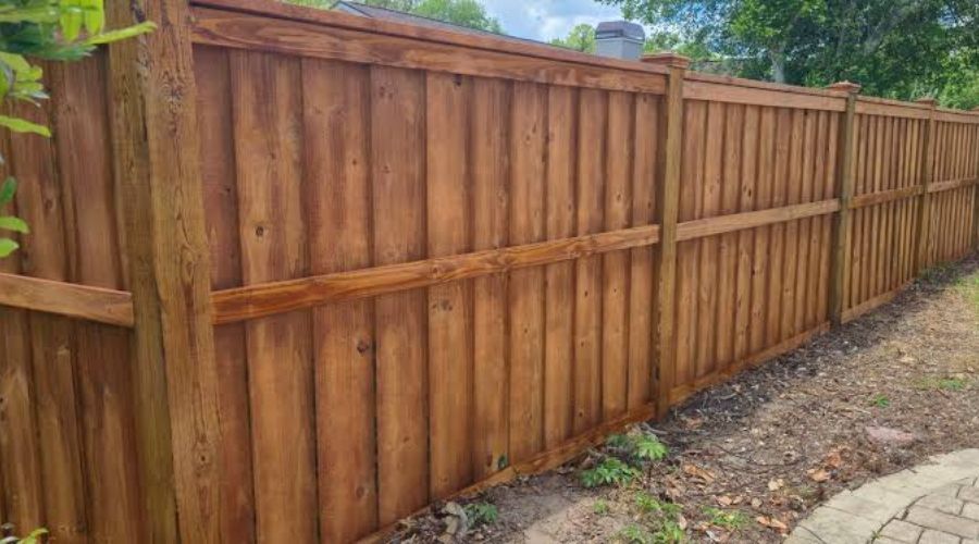 Stained wood board-on-board privacy fence with top cap rail.