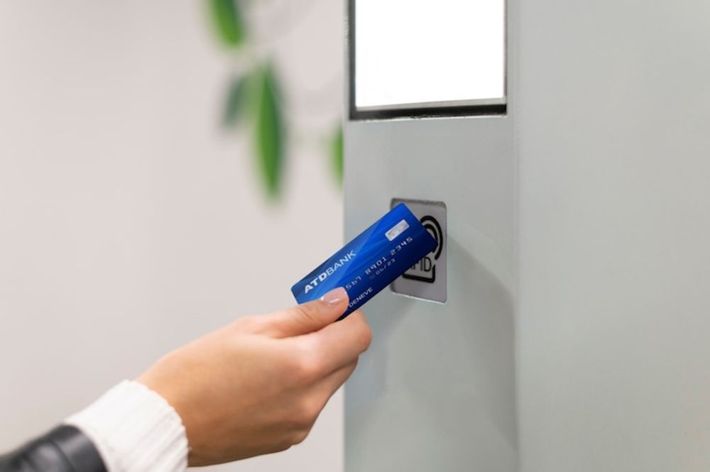 Fingerprint scanner on black door; person's finger on sensor, displaying blue digital image and red scan line.