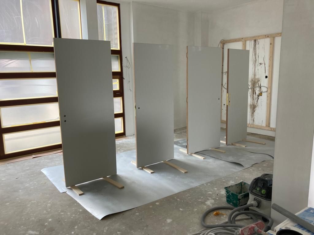 Vier grijze deuren staan tegen een muur in een kamer in aanbouw, met gereedschap en materialen in de buurt.