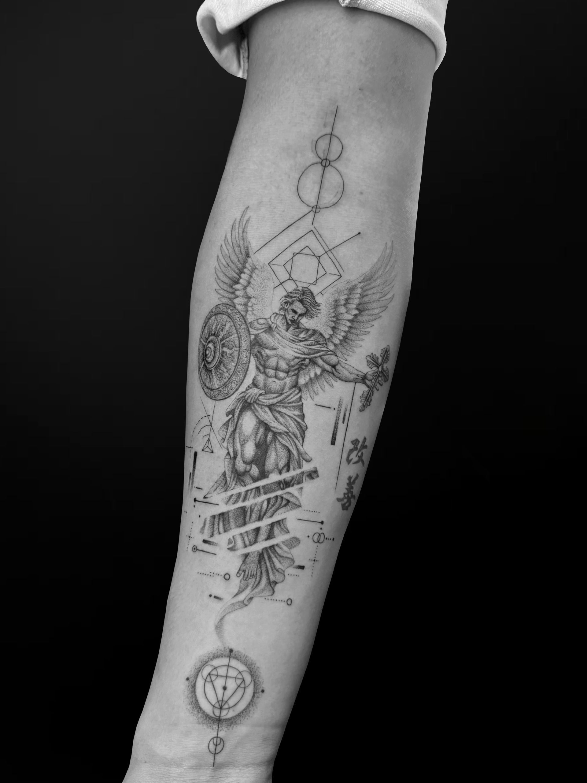 A forearm tattoo featuring a winged mythological figure, geometric shapes, and a circular emblem in a fine-line style.
