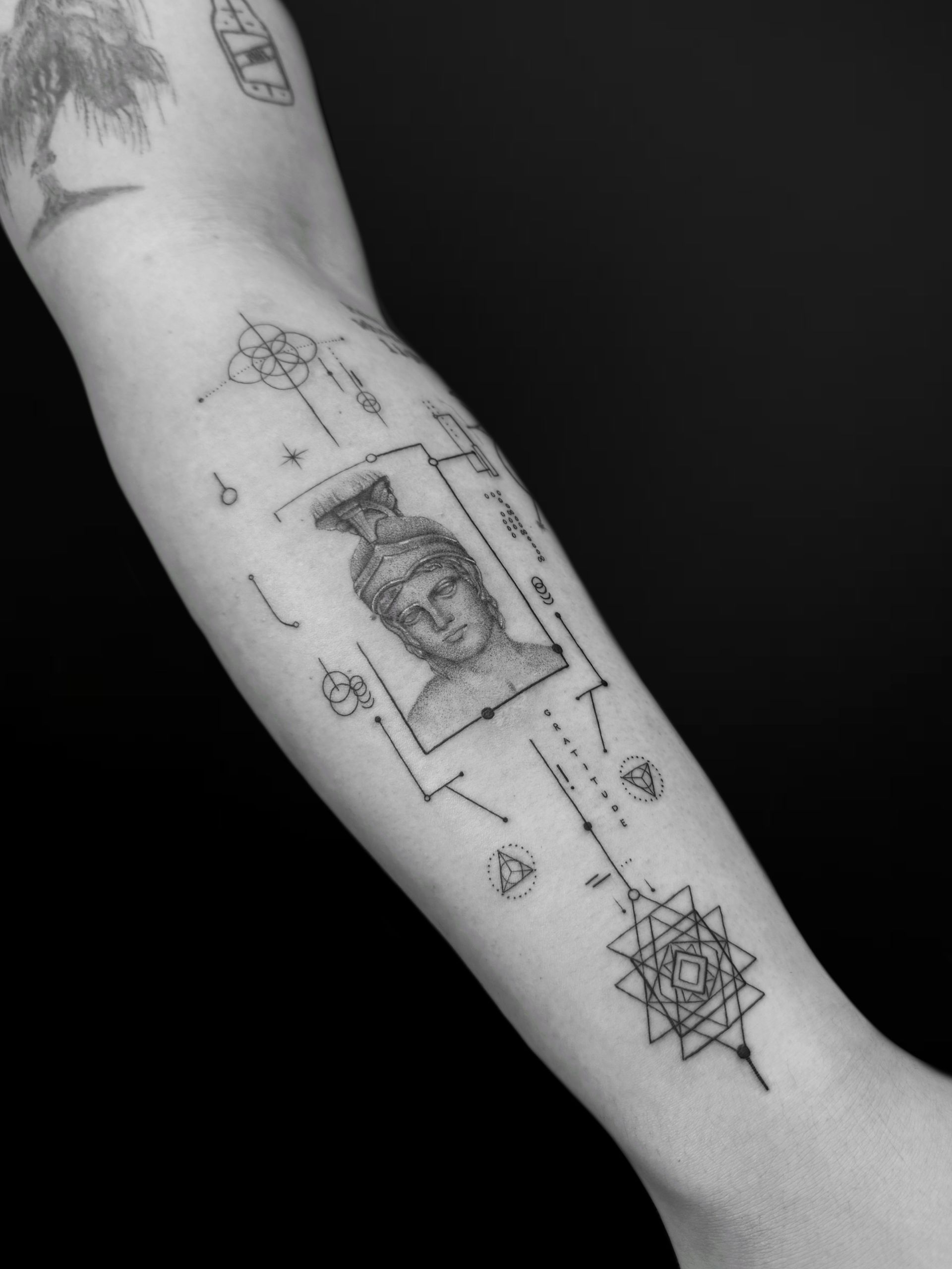 Fine-line forearm tattoo featuring a classical bust framed by geometric lines, symbols, and a complex star emblem.