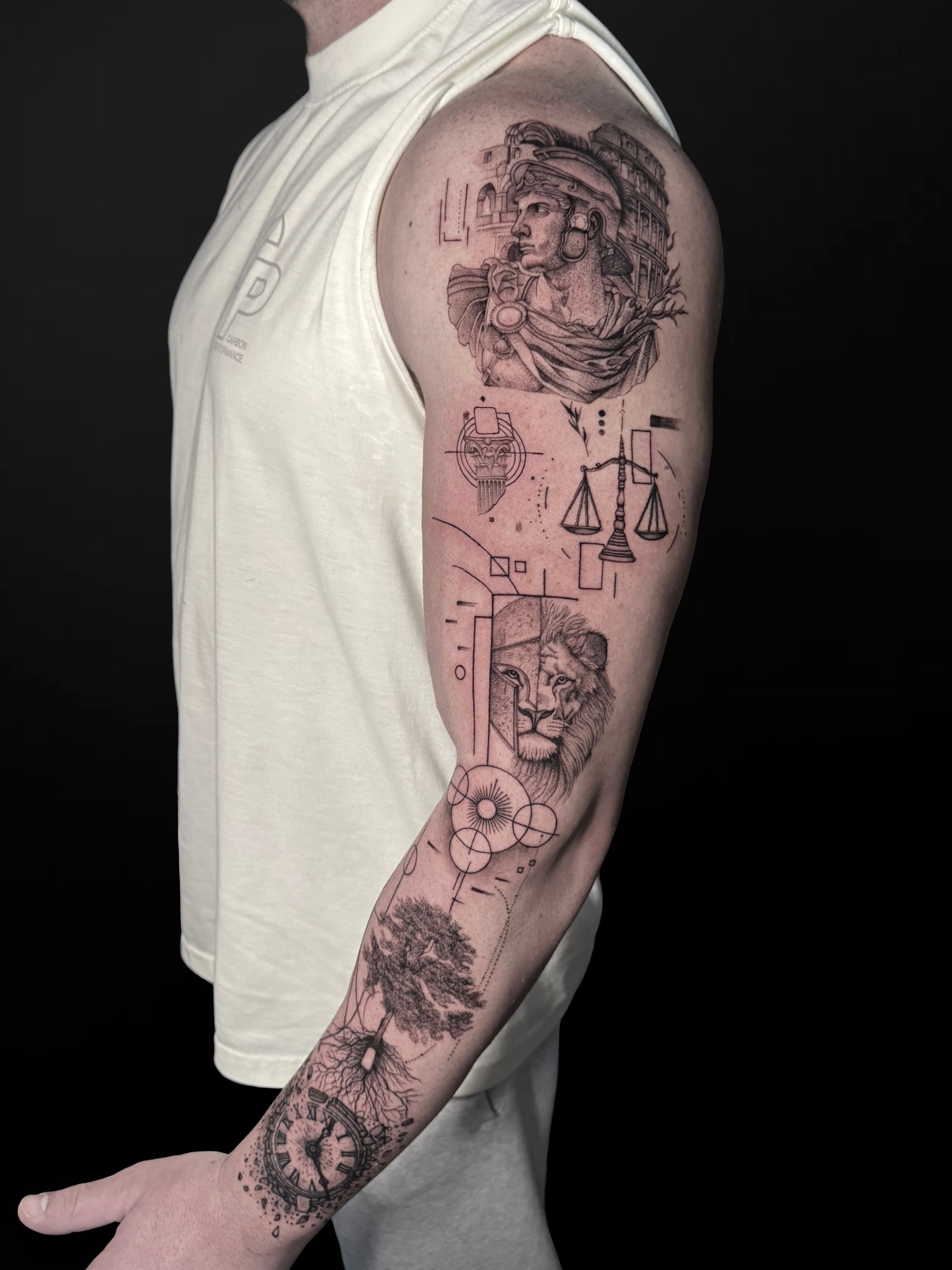 A black-and-white tattoo sleeve featuring a portrait, scales, a lion, geometric patterns, and clock motifs on an arm.