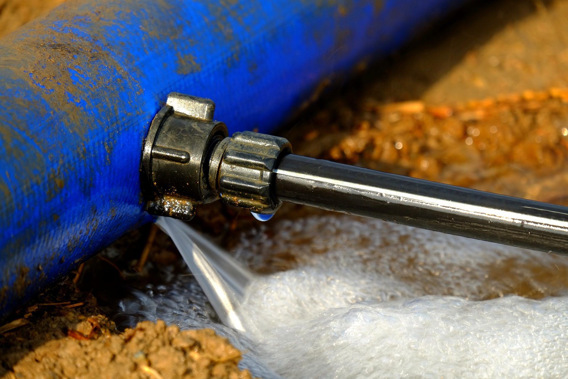 A blue pipe is leaking water and a hose is spraying water.