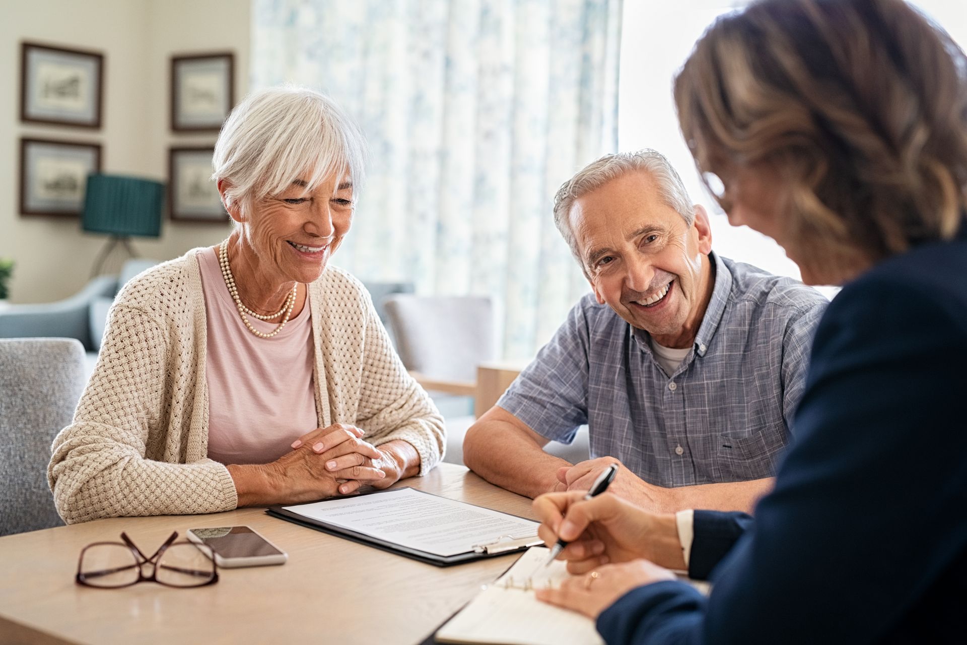 An elderly couple is sitting at a table talking to a woman.