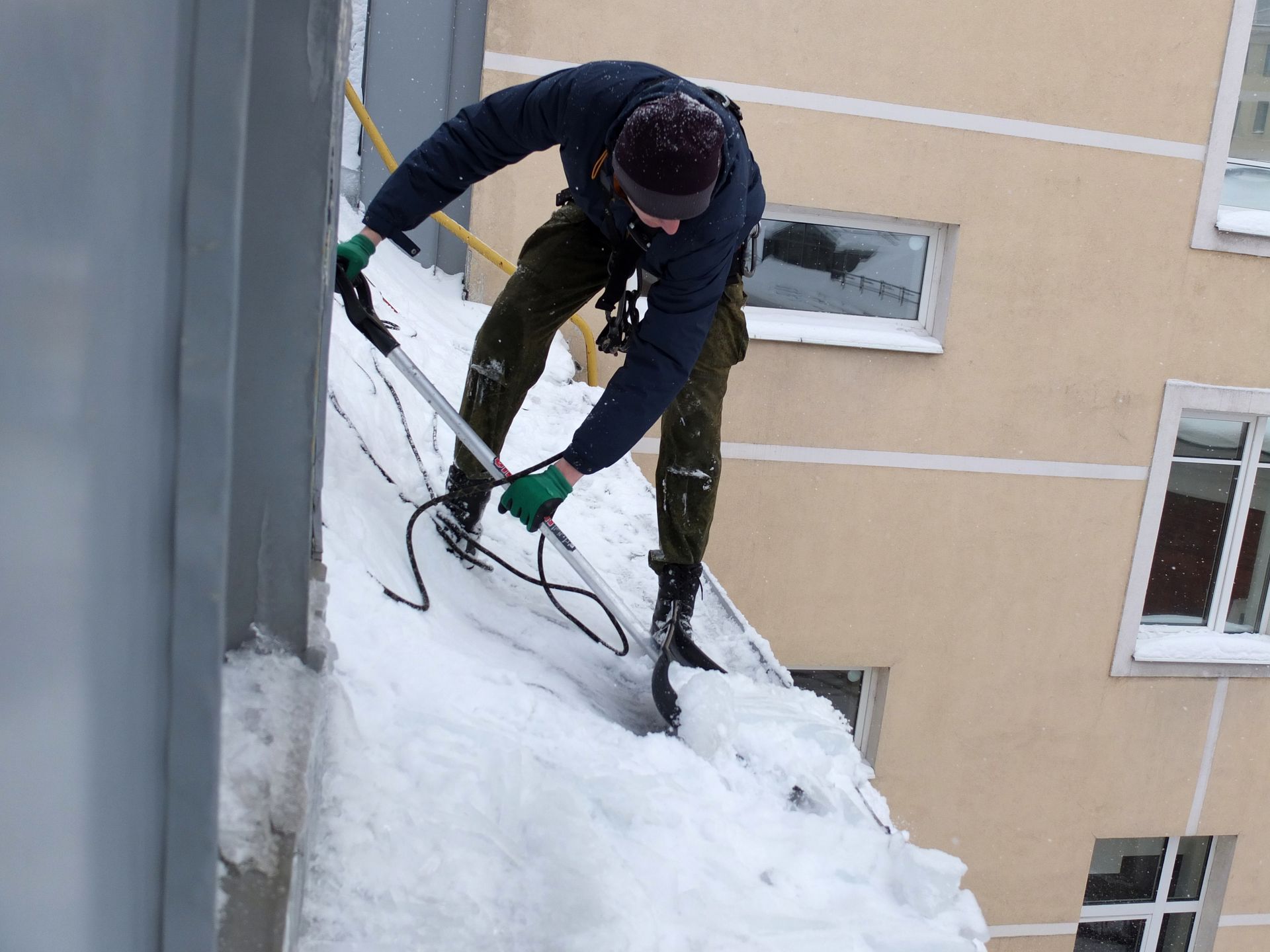 A man is shoveling snow from the side of a building.