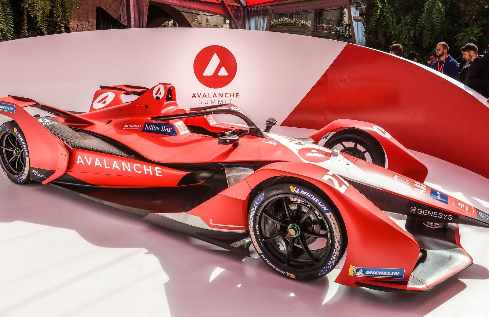 A bright red Avalanche Andretti Formula E race car sits on display in front of a matching branded backdrop.