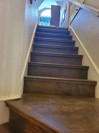 A set of dark wood-toned stairs leading upward toward a landing with a window and a doorway.