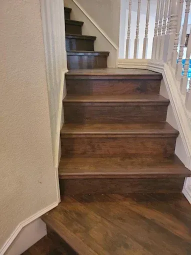 A view looking up at a dark wood staircase with white walls and a white balustrade on the right.