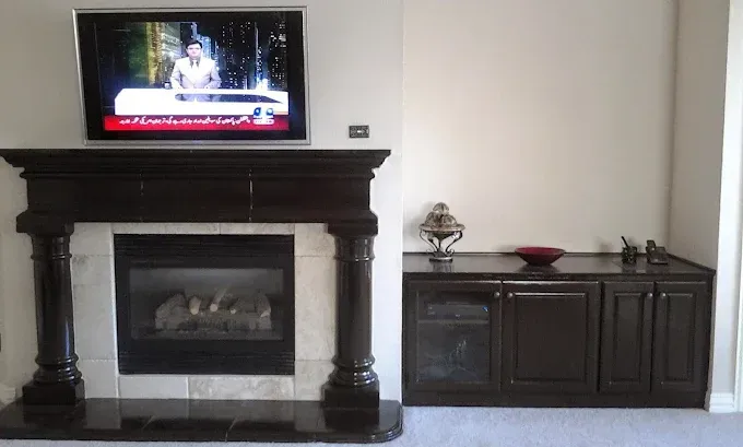 A flat-screen TV mounted above a dark wood fireplace, next to a matching dark wood cabinet with decorative items on top.