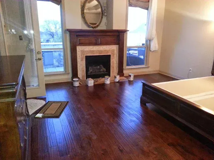 A bedroom with dark wood floors, a wooden fireplace, an oval mirror, and a bed frame.