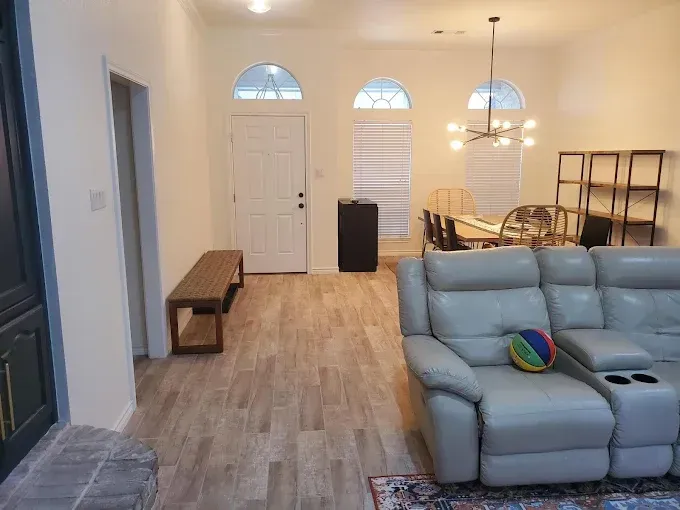 A bright open-concept living area with wood-look flooring, a gray sectional sofa, a wooden bench, and a dining set.