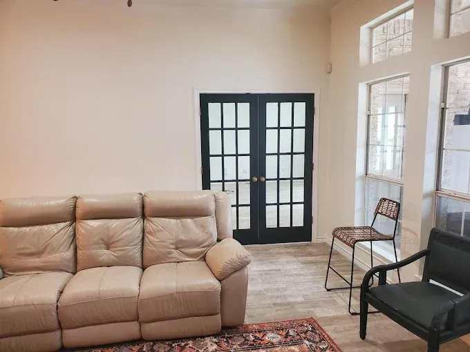 A light-colored leather sofa sits next to a black armchair and a tall stool in a room with black-framed French doors.