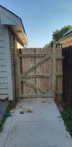 A newly installed wooden gate with a diagonal brace, positioned between a house wall and an existing wood fence.
