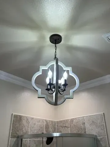 A four-light chandelier with a white quatrefoil frame hanging above a tiled shower in a bathroom.