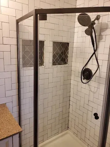 A glass-enclosed shower with white subway tiles in a herringbone pattern, two small wall niches, and matte black fixtures.