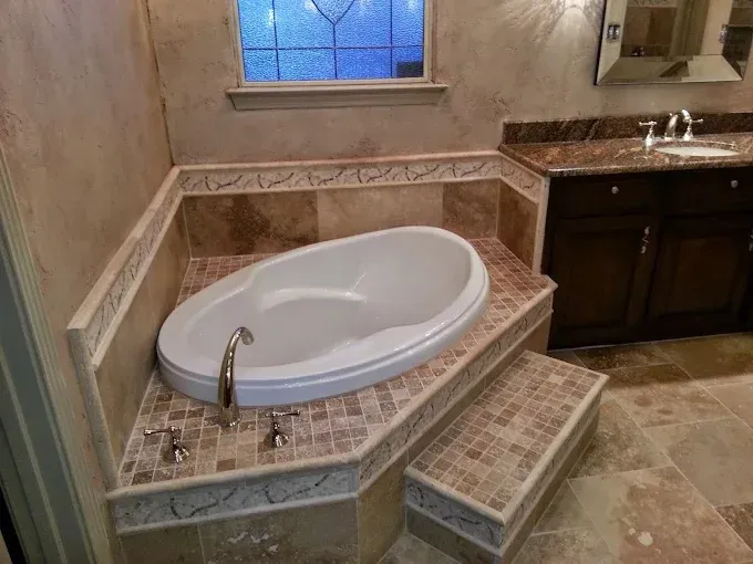 A built-in white oval bathtub with tile surround, a small step, and an adjacent dark wood vanity in a bathroom.