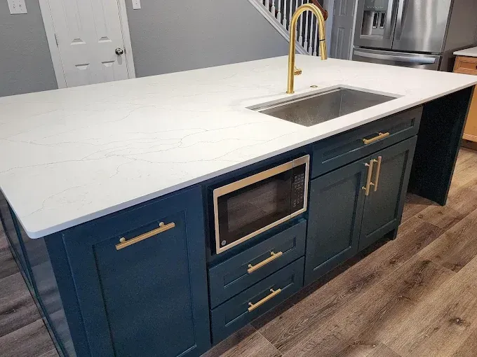 A kitchen island with dark blue cabinets, gold hardware, a white quartz countertop, and an integrated microwave.
