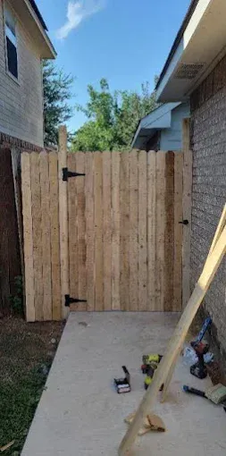A newly installed wooden fence gate between two houses, with tools and wood scraps on the concrete patio.
