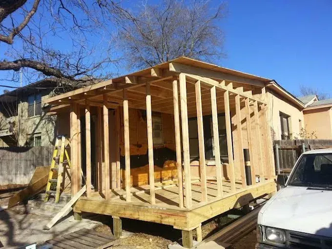 A wooden frame of an addition to a residential house under construction, with a ladder leaning against the side.