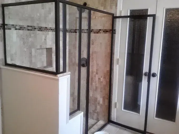 A walk-in shower with black-framed glass walls and a tiled interior, positioned next to a white door with glass panels.