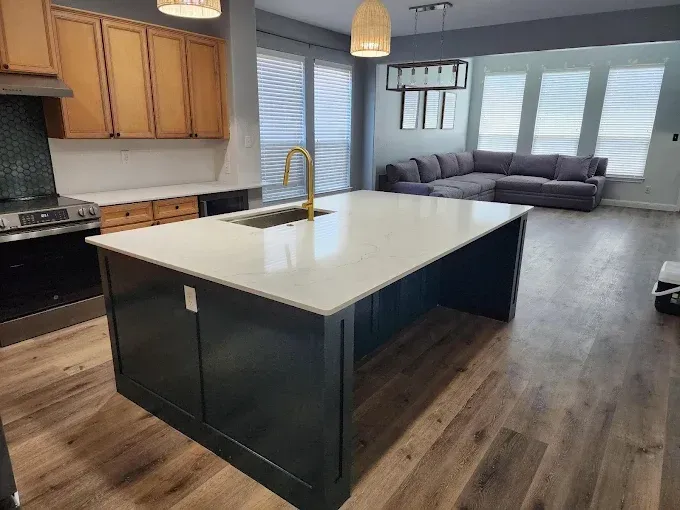A spacious modern kitchen featuring a dark blue island with a white countertop and a living room area in the background.