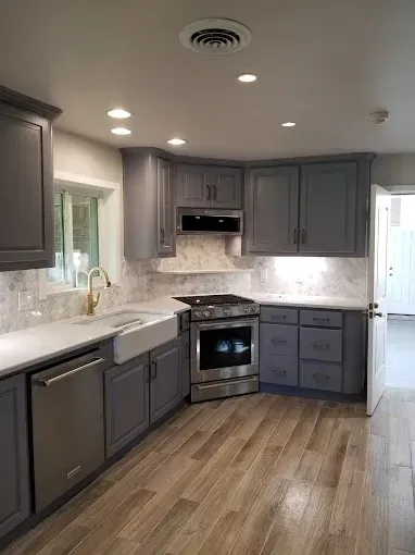 Modern kitchen with gray cabinets, a white farmhouse sink, stainless steel appliances, and a marble backsplash.