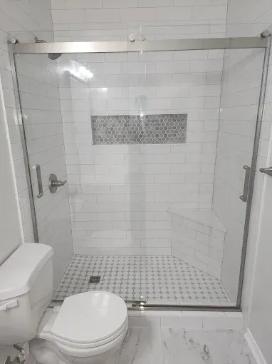 A modern bathroom featuring a white tiled glass shower with a built-in corner seat and mosaic niche, next to a toilet.