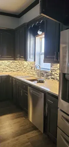 A kitchen featuring dark wood cabinets, a textured stone backsplash, granite countertops, and stainless steel appliances.