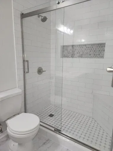 A modern bathroom with a white toilet and a glass-enclosed shower featuring white subway tiles and a stone-tiled inlay.