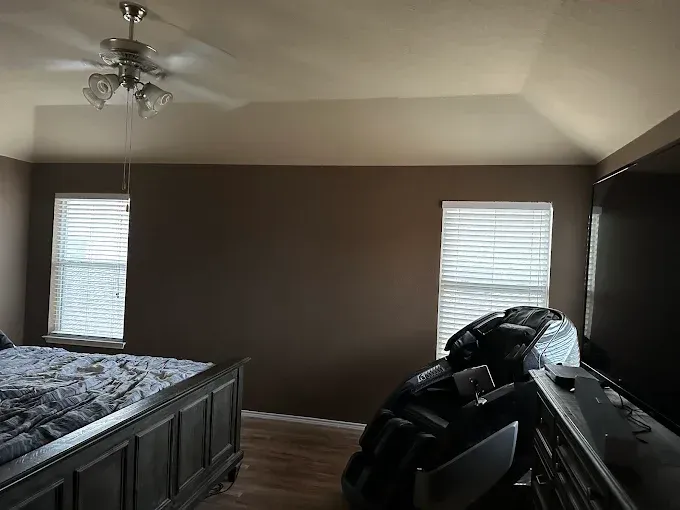A bedroom with a tray ceiling, brown walls, two windows with blinds, a dark wooden bed frame, and a large massage chair.