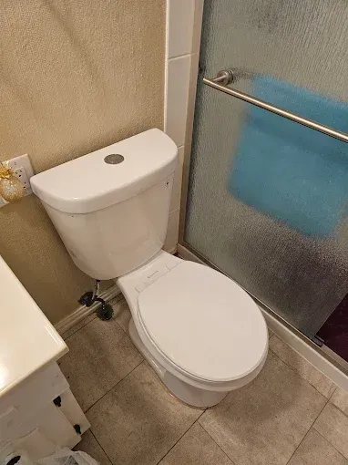 A white toilet with a lid down in a bathroom, situated next to a glass-paneled shower door and a vanity.