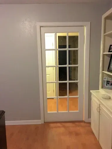 A white 15-pane glass door in a grey room with light wood flooring and a white cabinet to the right.