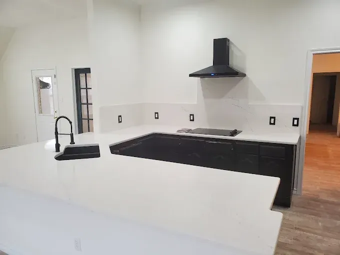 A modern kitchen featuring dark cabinets, a large white countertop island, and a black range hood against white walls.