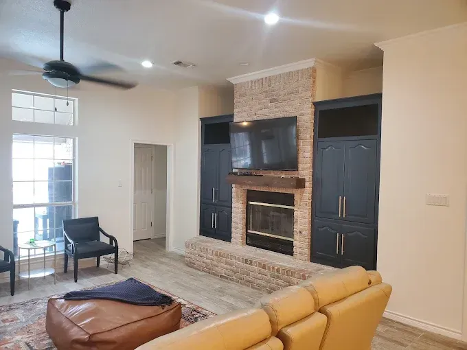 A modern living room with a stone fireplace, dark blue built-in cabinets, a leather ottoman, and a tan sofa.