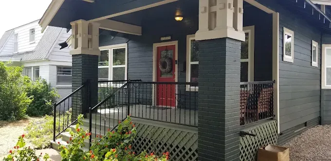 A front porch of a dark gray house with a bright red front door, black railings, and stone-style columns.