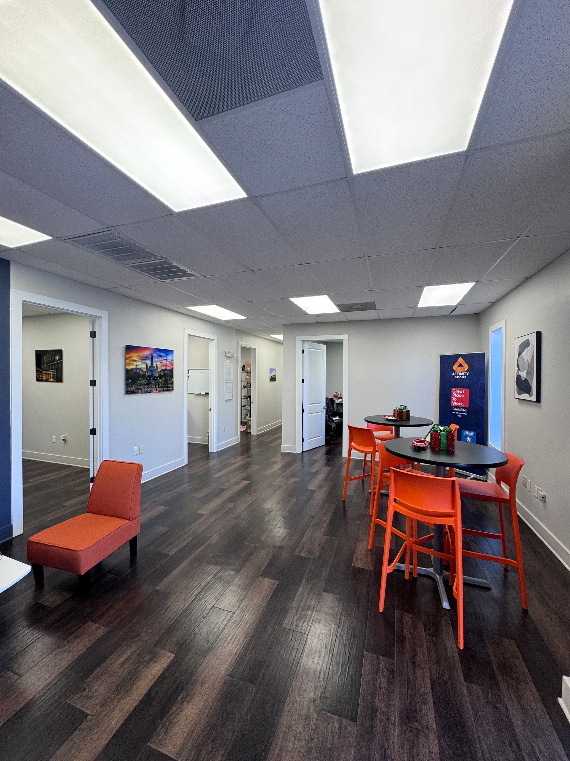 Modern office lounge with orange chairs, dark wood floor, white walls, and fluorescent ceiling lights