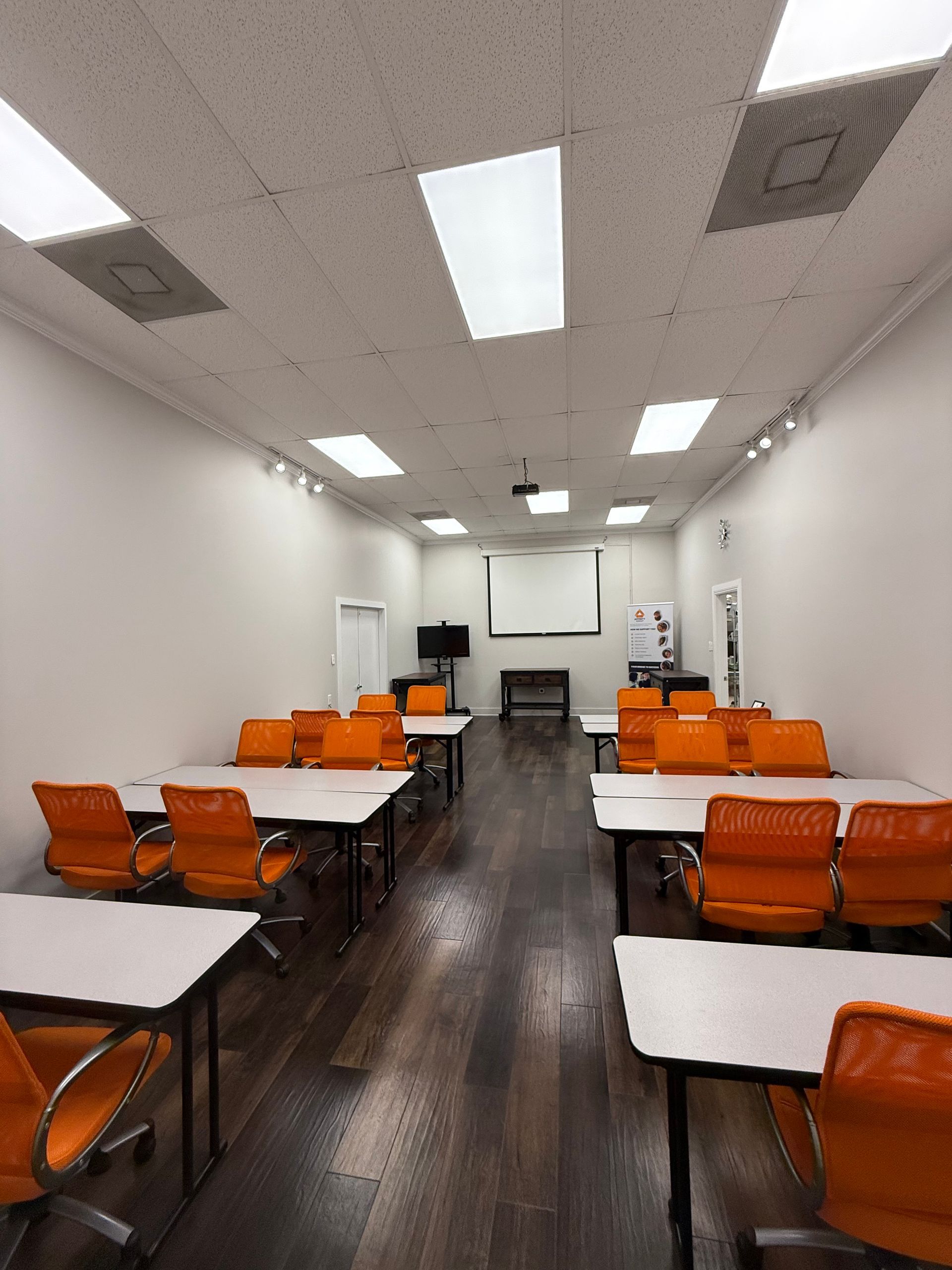 Empty classroom with rows of orange chairs and white desks, projector screen at the front