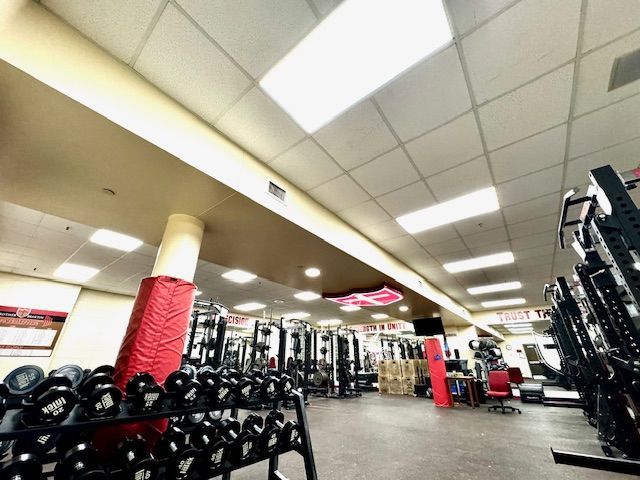 Gym interior with dumbbell racks, weight machines, and bright fluorescent ceiling lights