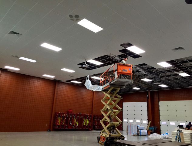Maintenance worker in orange lift repairing ceiling lights in a large room with red walls