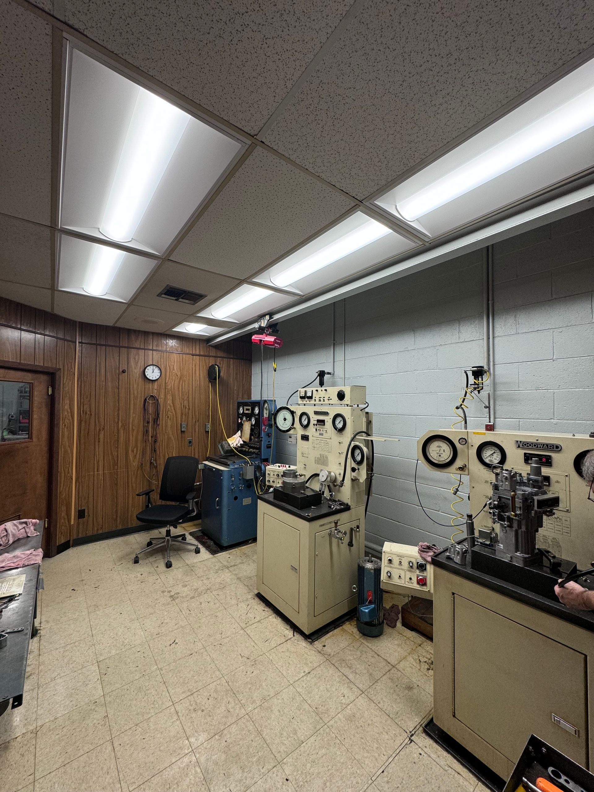 Industrial room with two beige machines, wood-paneled wall, and bright fluorescent ceiling lights.