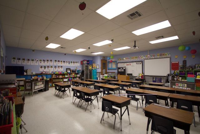 Empty classroom with rows of student desks, colorful walls, and bright fluorescent ceiling lights.