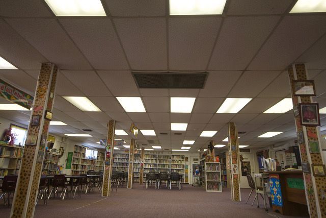 Wide interior of a library with bookshelves, tables, and bright fluorescent ceiling lights