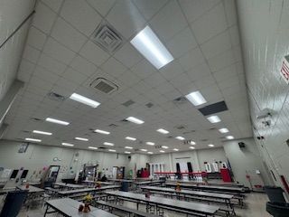Large cafeteria with long tables and benches under bright ceiling lights.