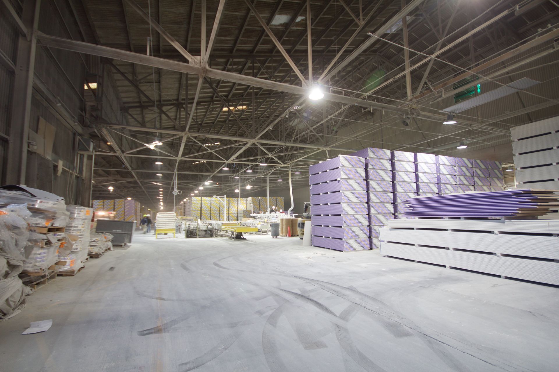 Snow-covered warehouse interior with stacked purple-wrapped pallets and overhead lights